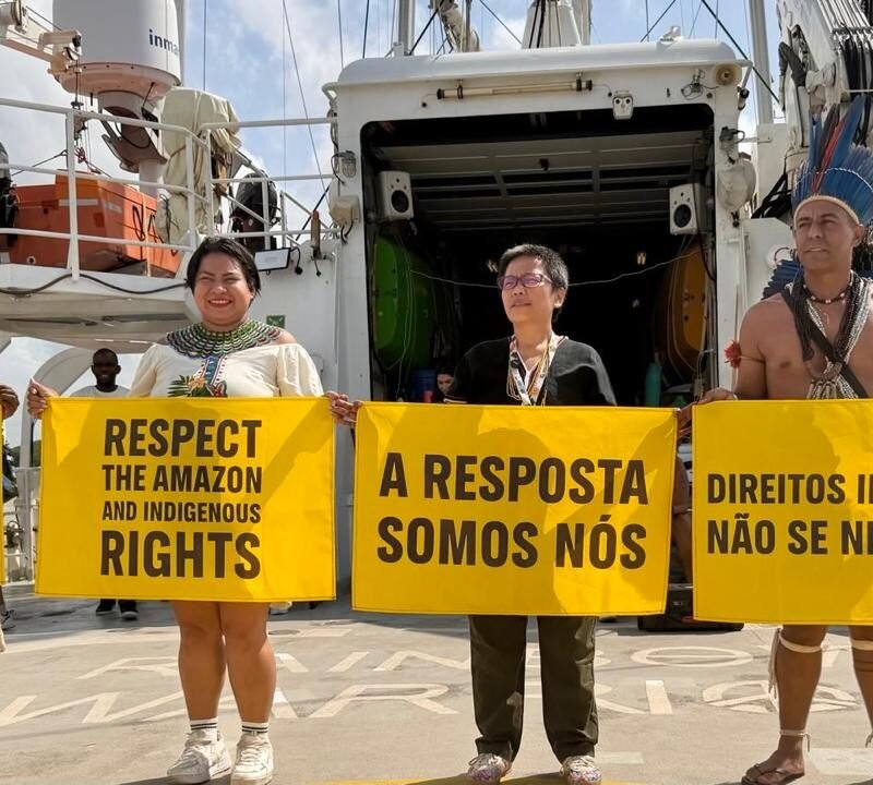 Sekretaris Jenderal AMAN, Rukka Sombolinggi (kedua dari kanan) dan perwakilan Masyarakat Adat Papua, Fransiska Rosari Clarita You (paling kiri) membentangkan poster menentang perusakan hutan di atas Rainbow Warrior, kapal milik Greenpeace di Sungai Amazon pada 12 November 2025. (Dokumentasi JustCOP)